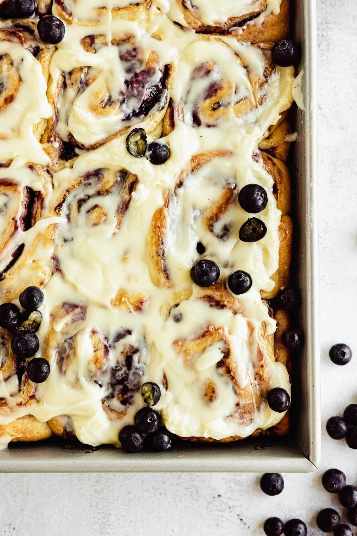 baking pan with cinnamon rolls, fresh blueberries, and cream cheese frosting