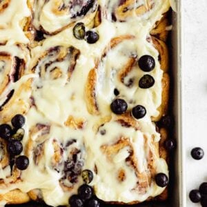 baking pan with cinnamon rolls, fresh blueberries, and cream cheese frosting