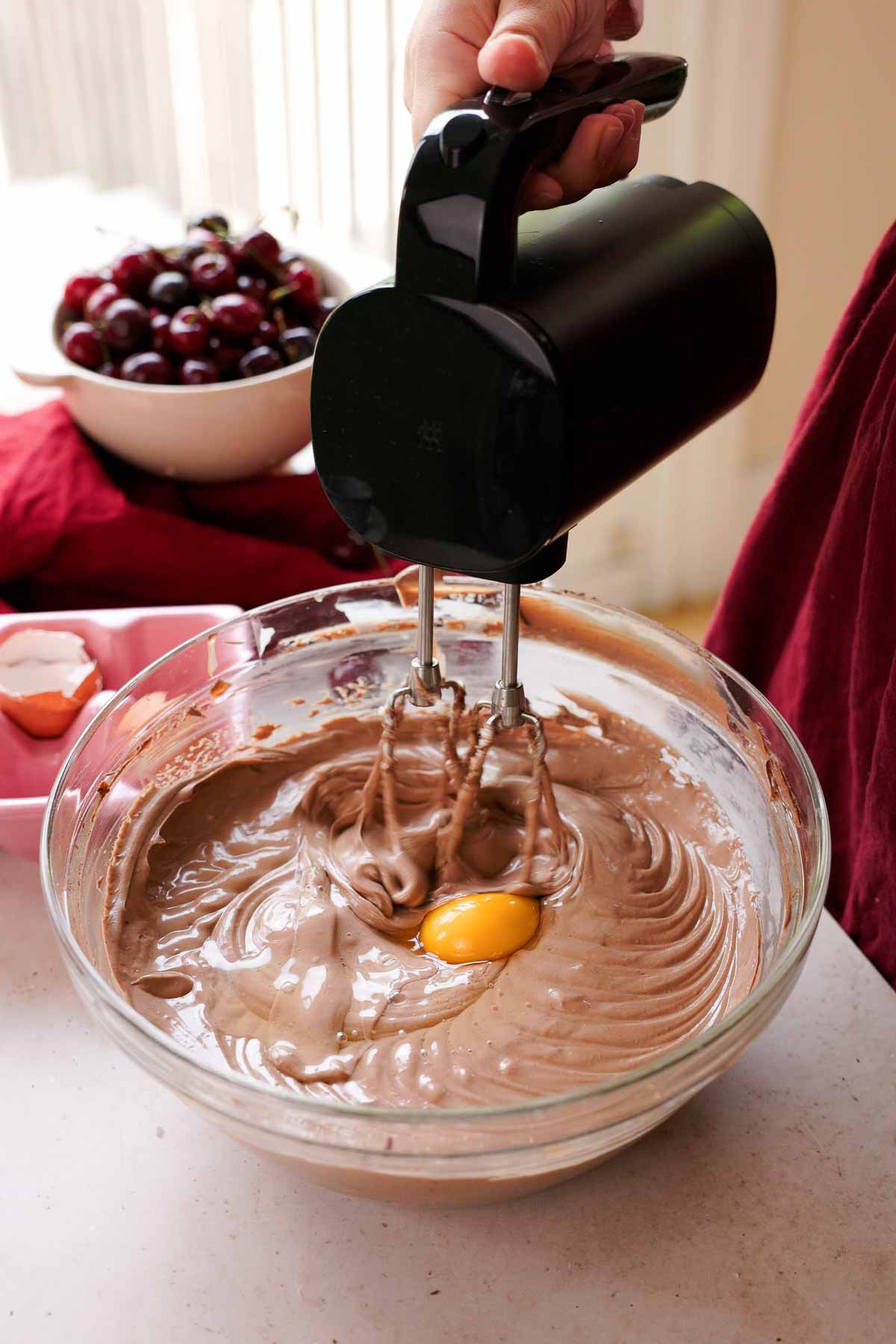adding eggs into chocolate cheesecake batter one by one