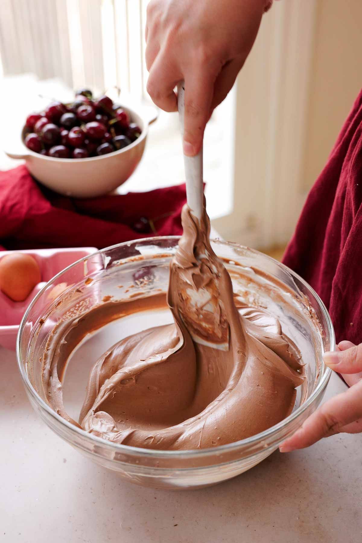 folding chocolate cheesecake batter with spatula in large glass bowl