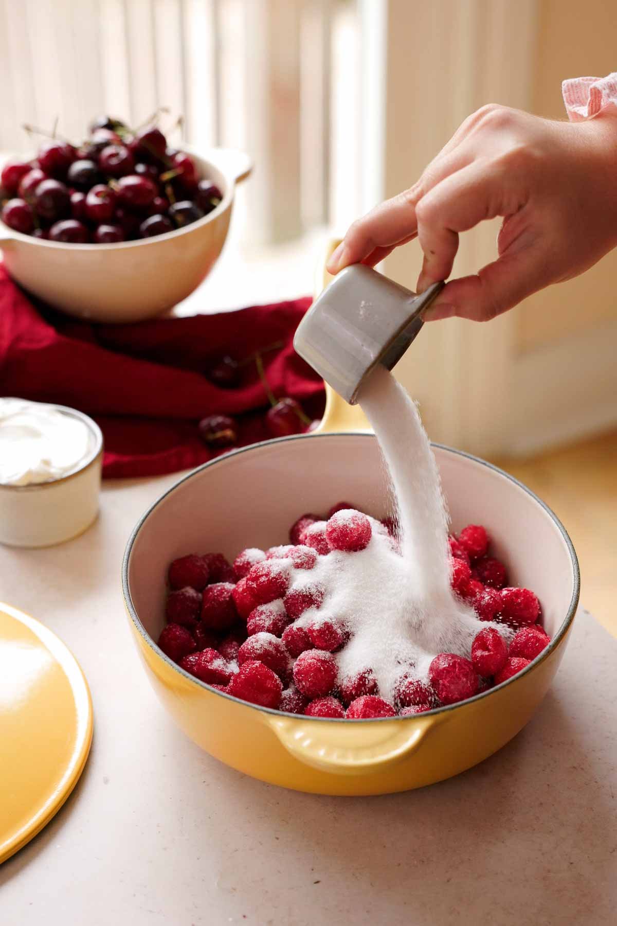 pouring sugar into frozen tart cherries in saucepan