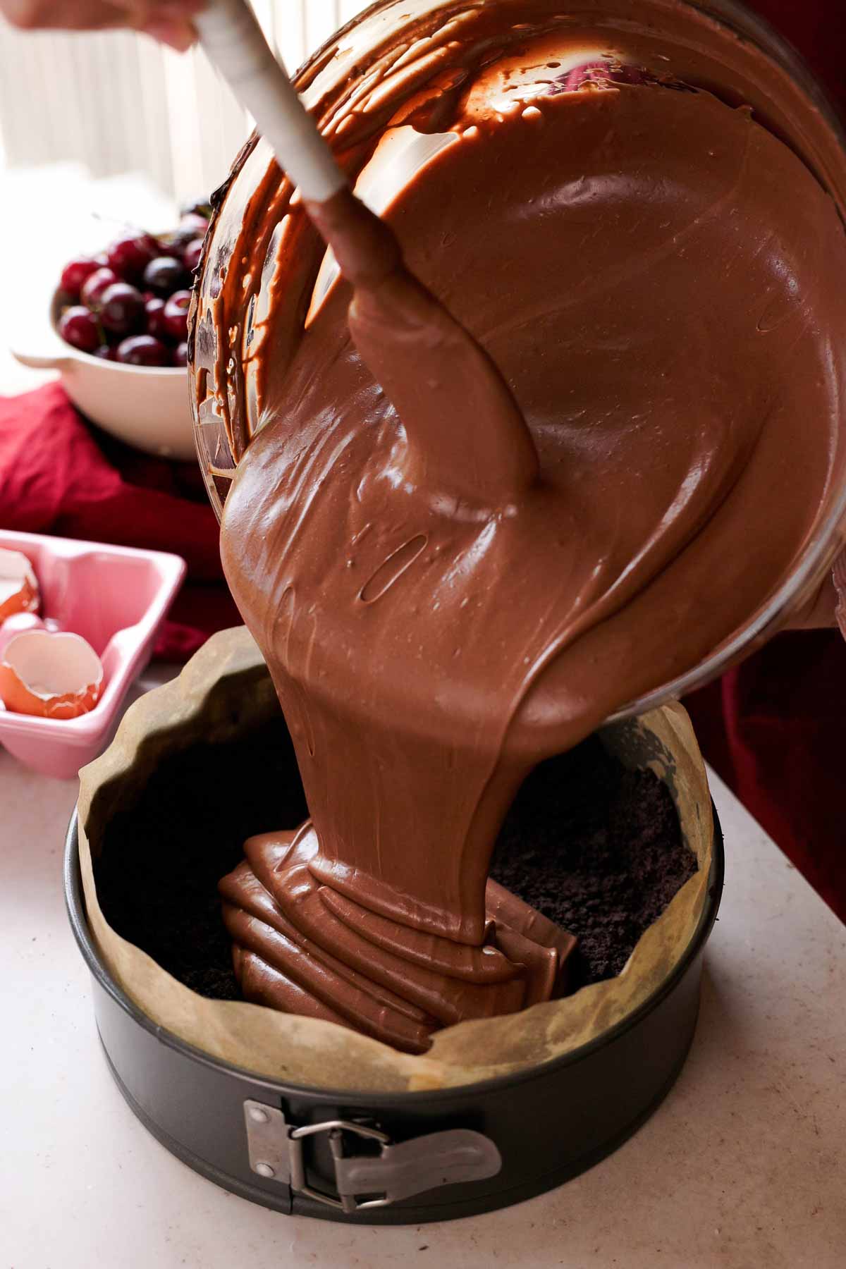 pouring chocolate cheesecake batter into oreo cheesecake crust