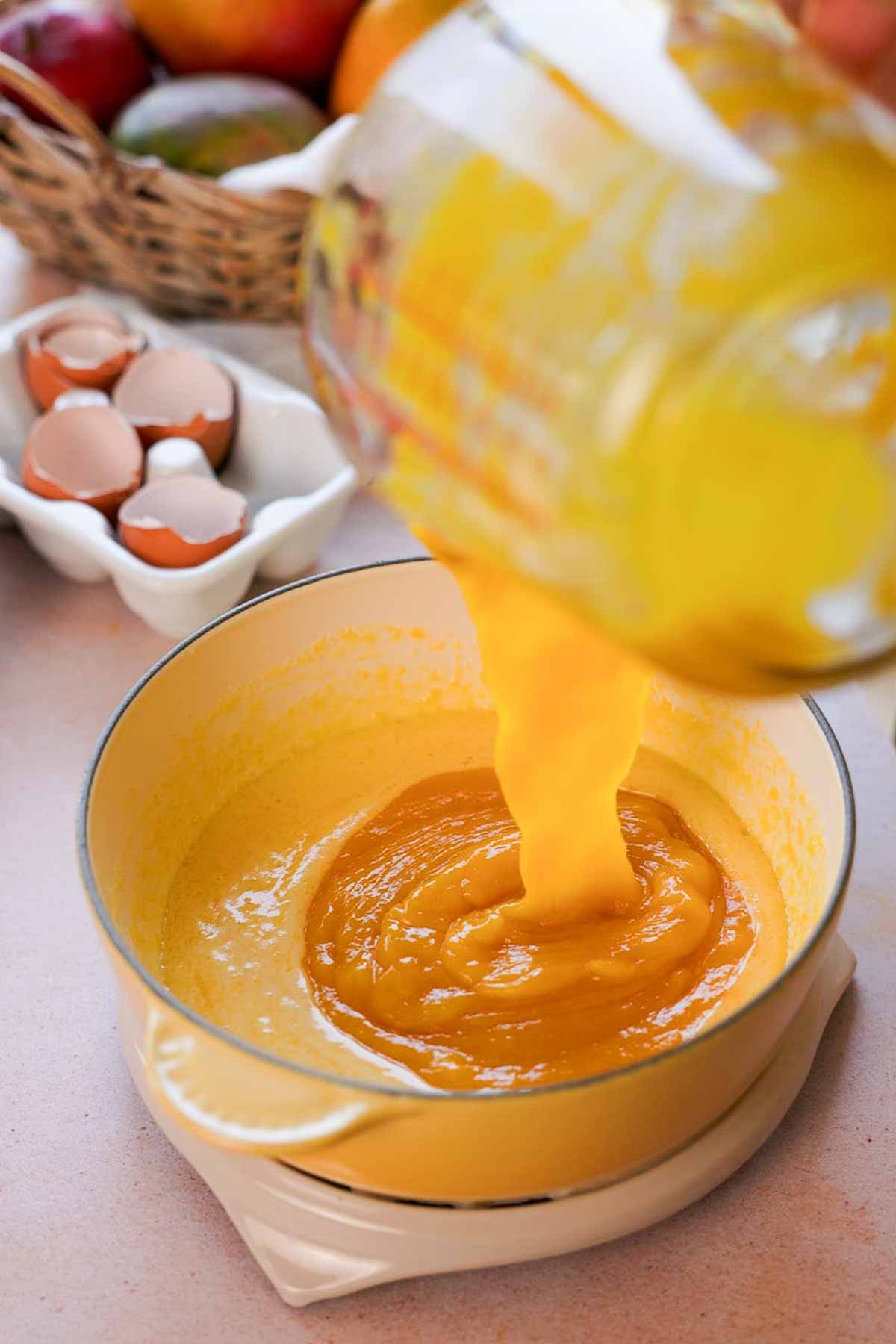 pouring mango puree into mango curd in saucepan