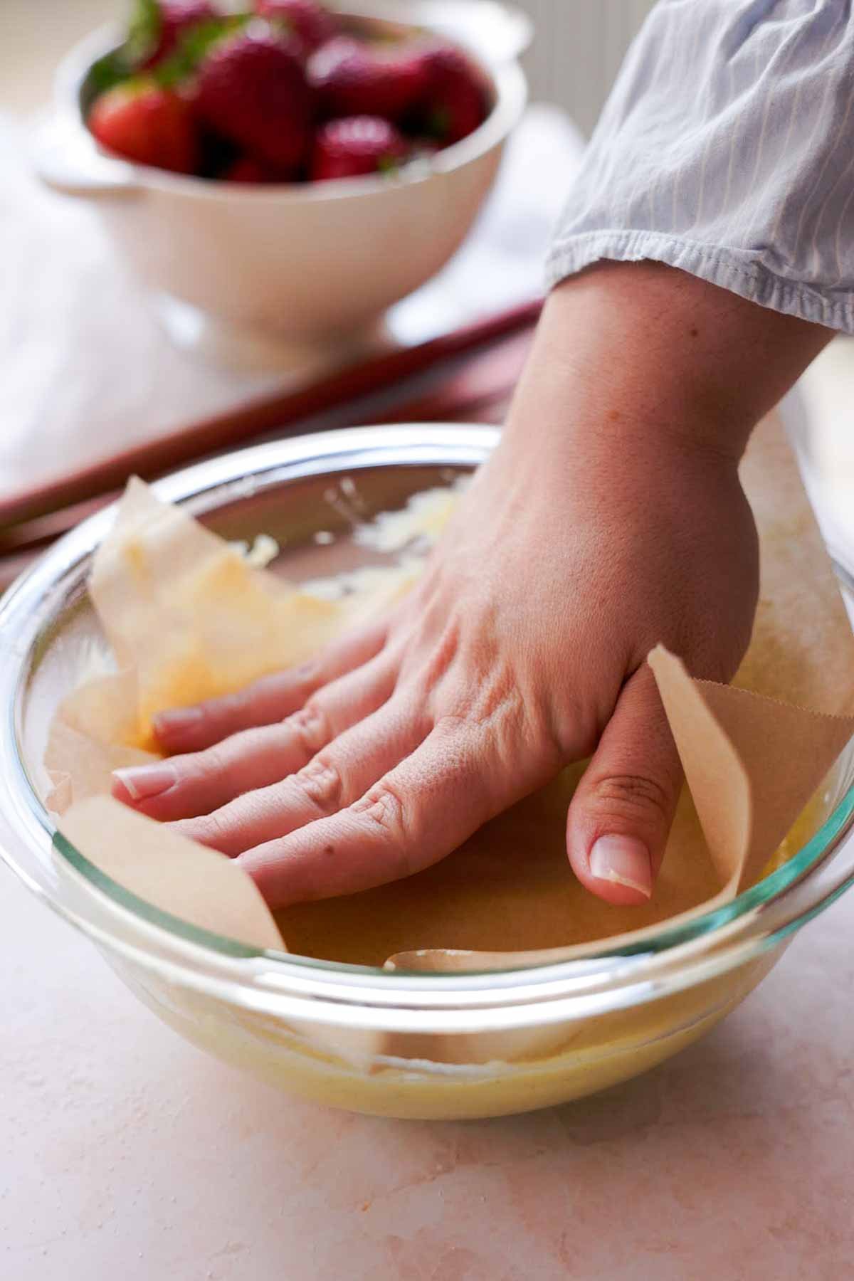 pressing down parchment paper onto bowl of hot custard