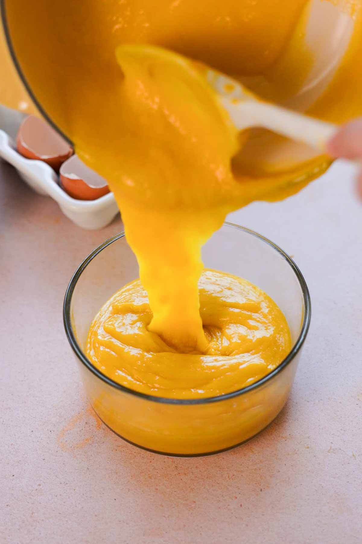 pouring mango curd into glass container to cool