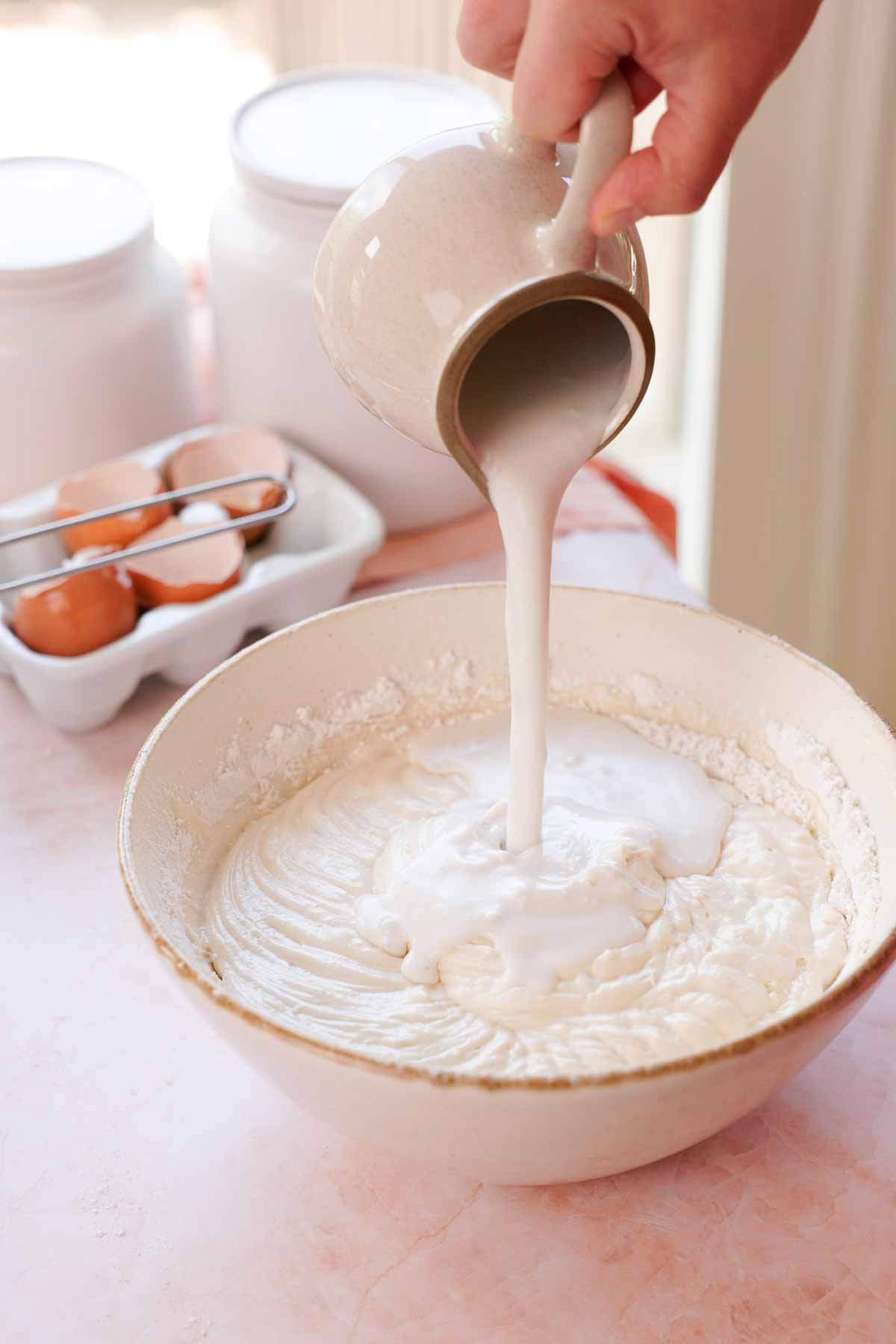 pouring coconut milk into coconut cake batter