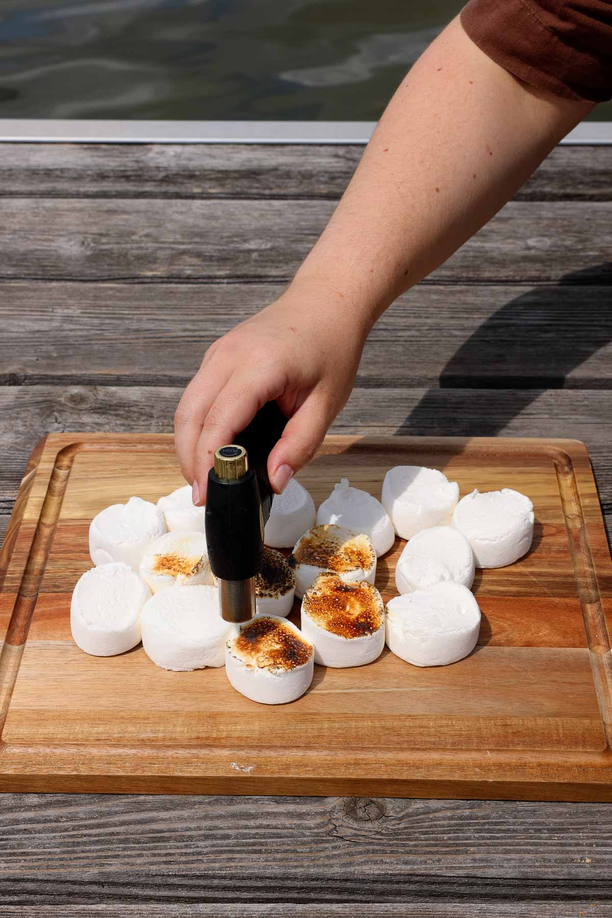 using a kitchen torch to roast marshmallows on wooden cutting board