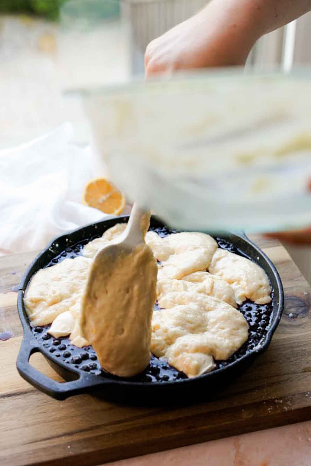 adding lemon cobbler batter onto blueberry cobbler