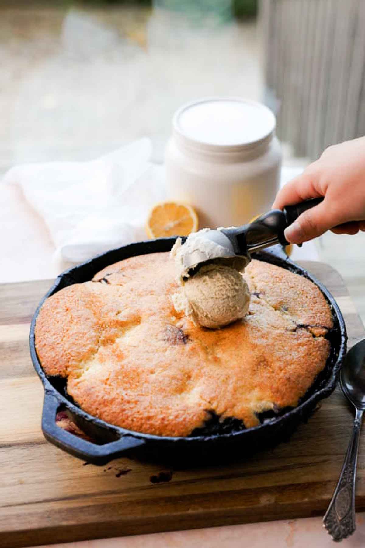 scooping vanilla ice cream onto blueberry lemon cream cheese cobbler