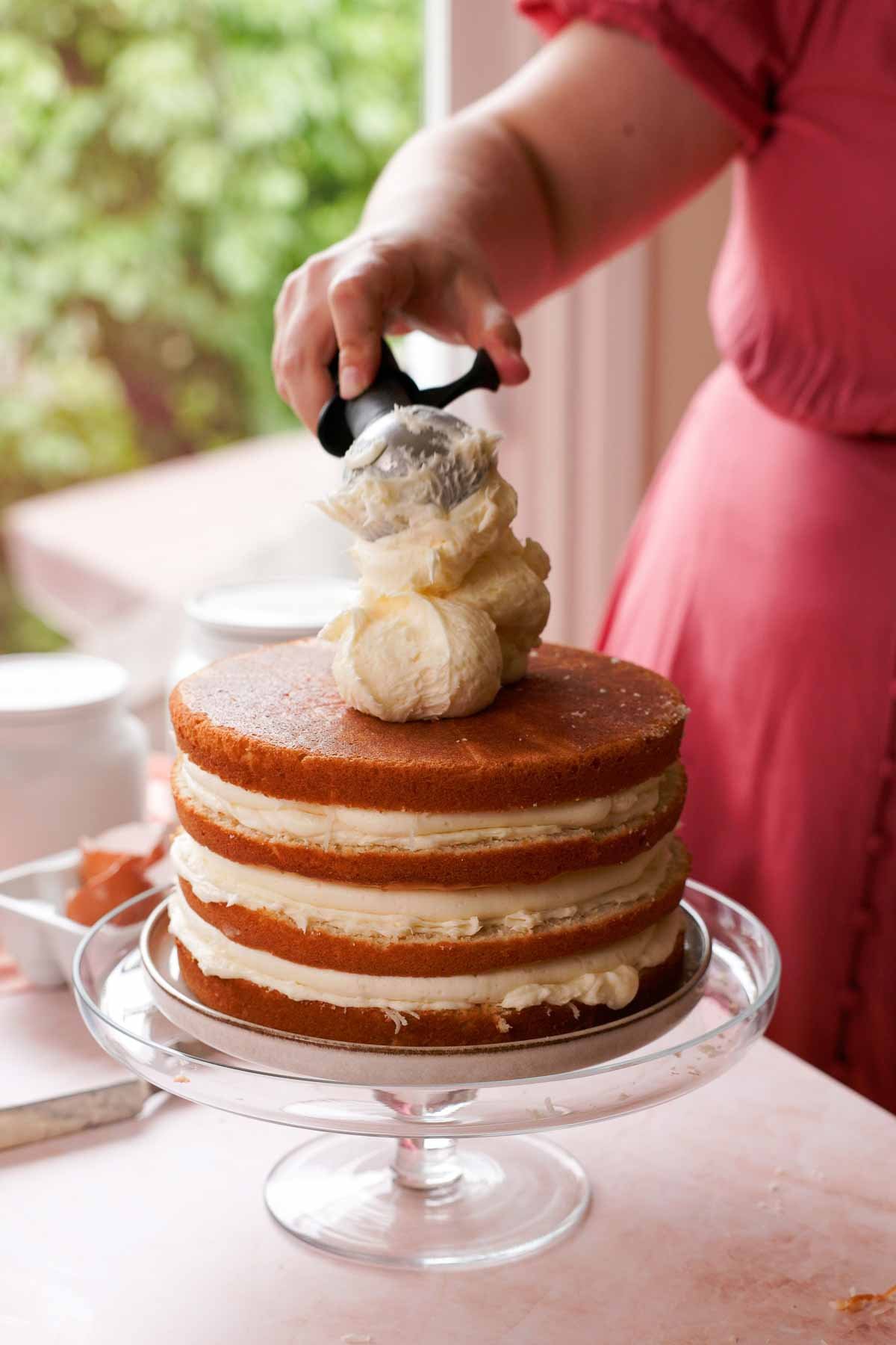 scooping coconut cream cheese frosting onto coconut cake