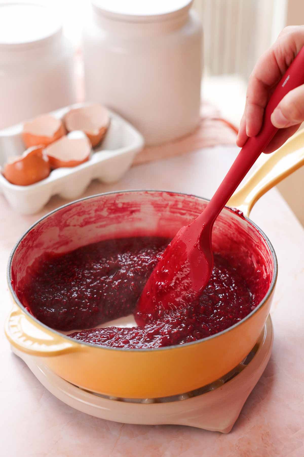stirring cooked and thickened raspberry cake filling in saucepan