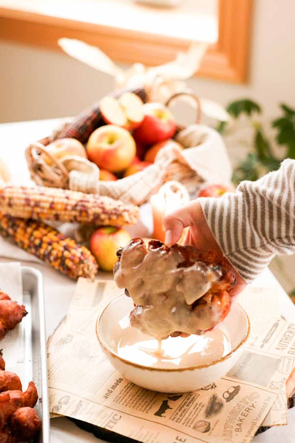 dipping apple fritters into a bowl with glaze