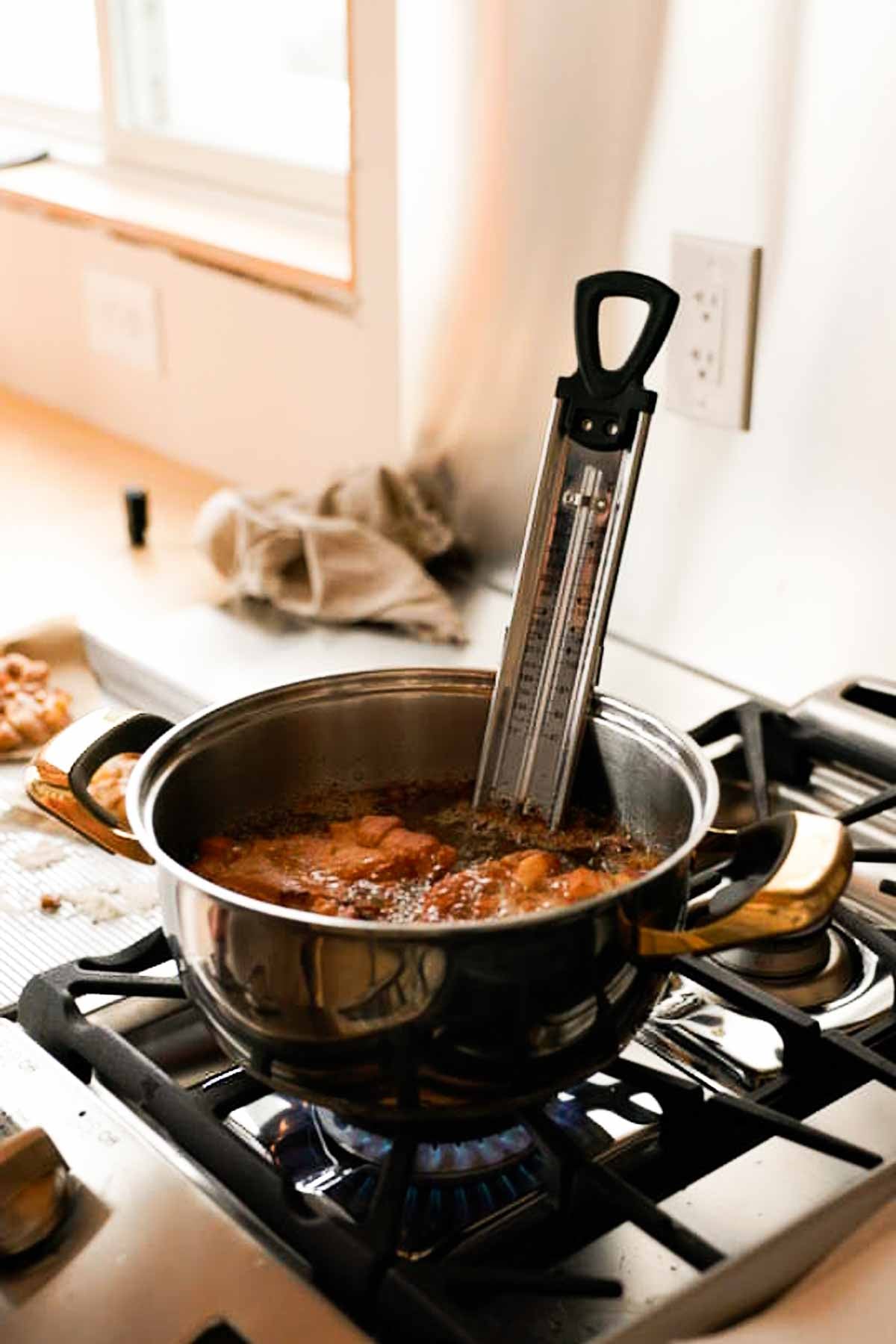 frying apple fritters in a pot filled with hot oil and a candy thermometer