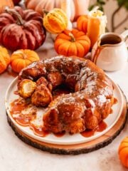 pumpkin monkey bread stuffed with cream cheese filling on a large plate with caramel sauce