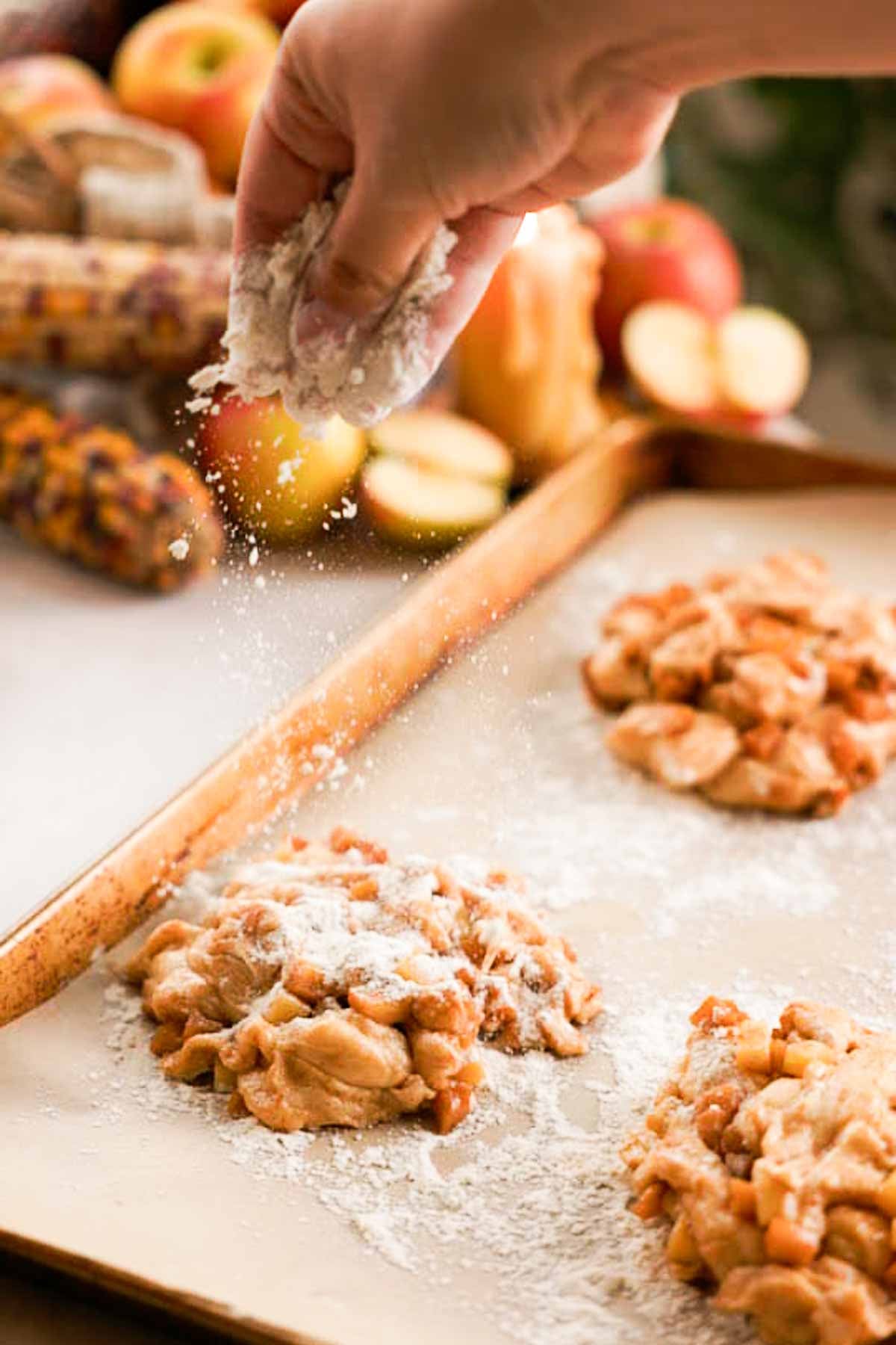sprinkling shaped apple fritters on parchment paper with flour