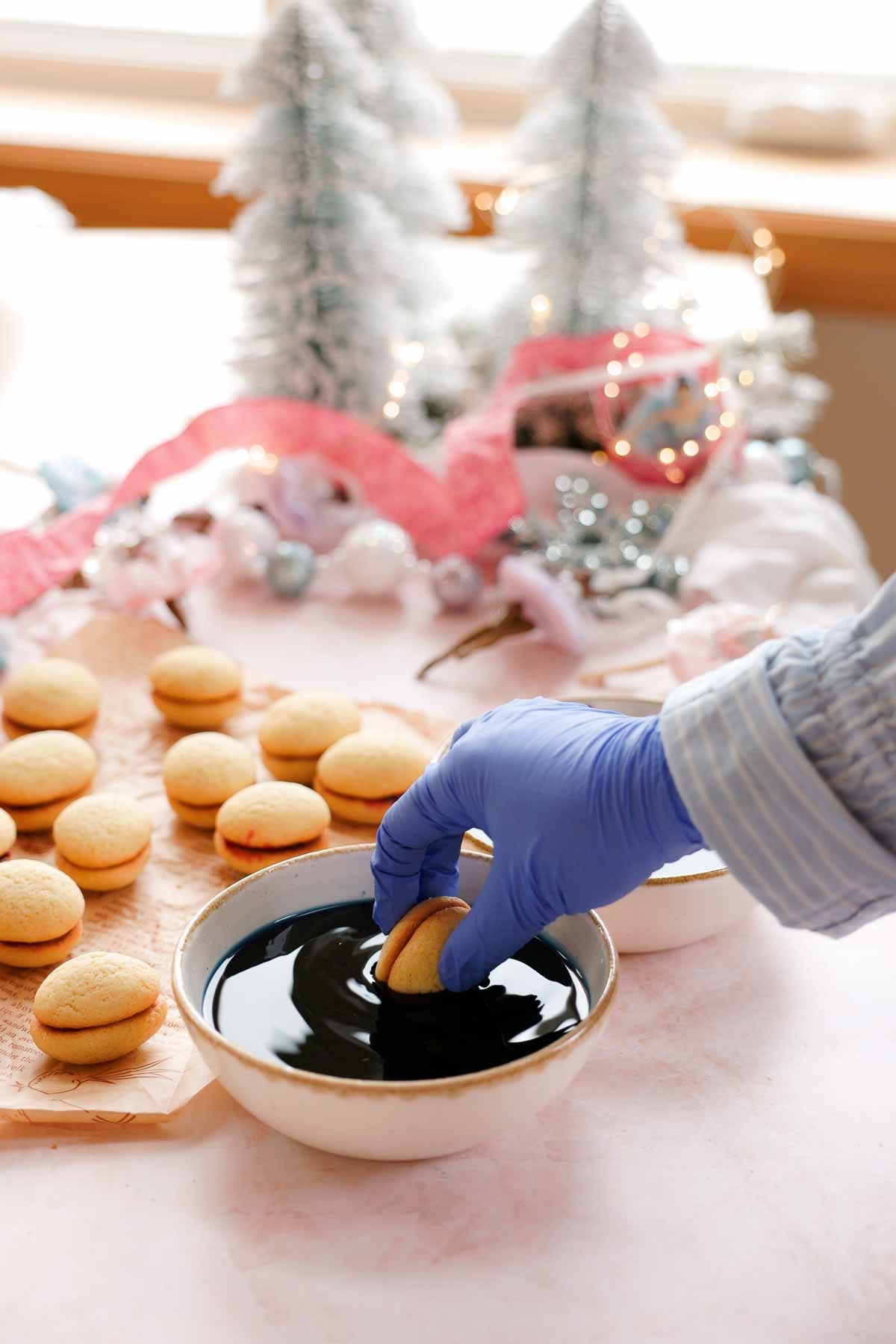 dipping filled sugarplum cookies into colored syrup, wearing gloves