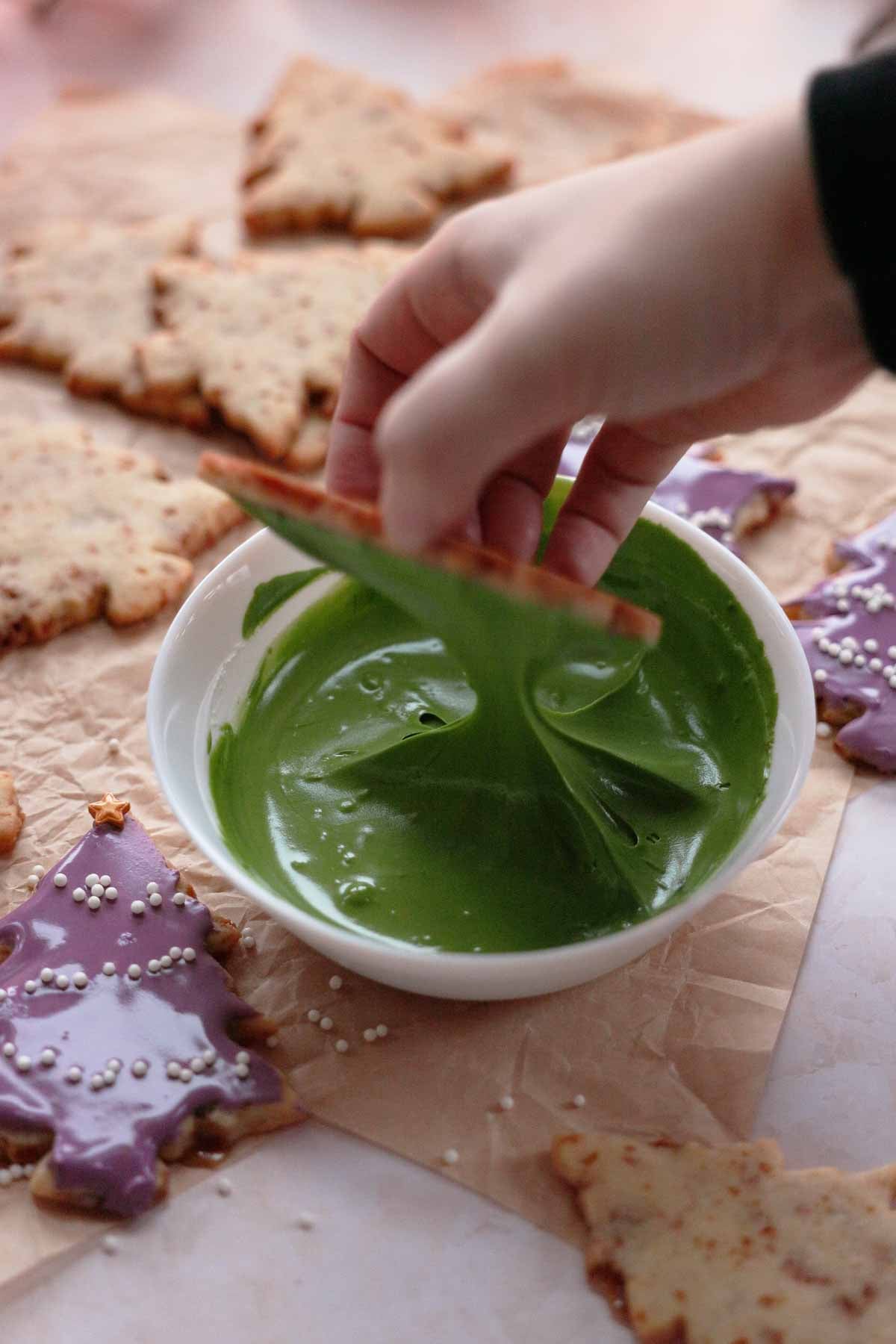 dipping caramel sugar cookies into a bowl of royal icing