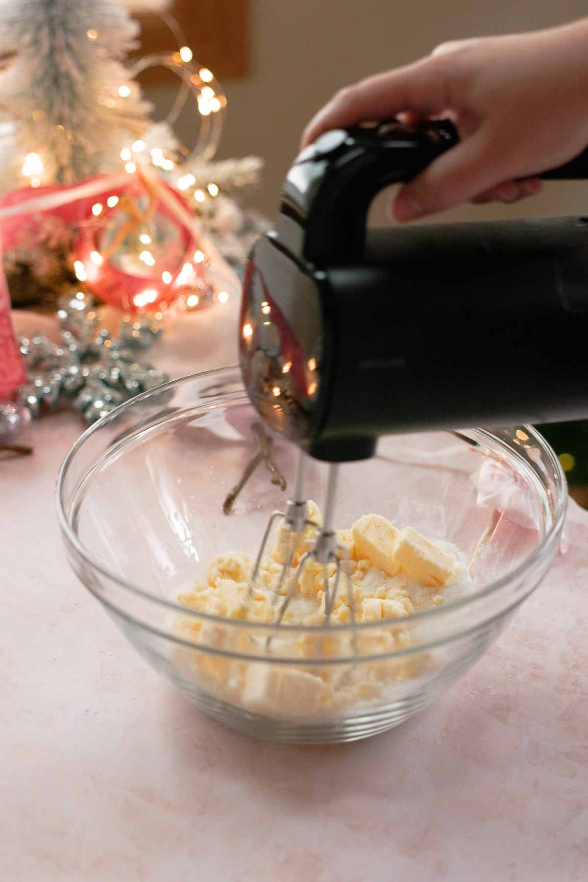 mixing butter and sugar in a large glass bowl with electric hand mixer