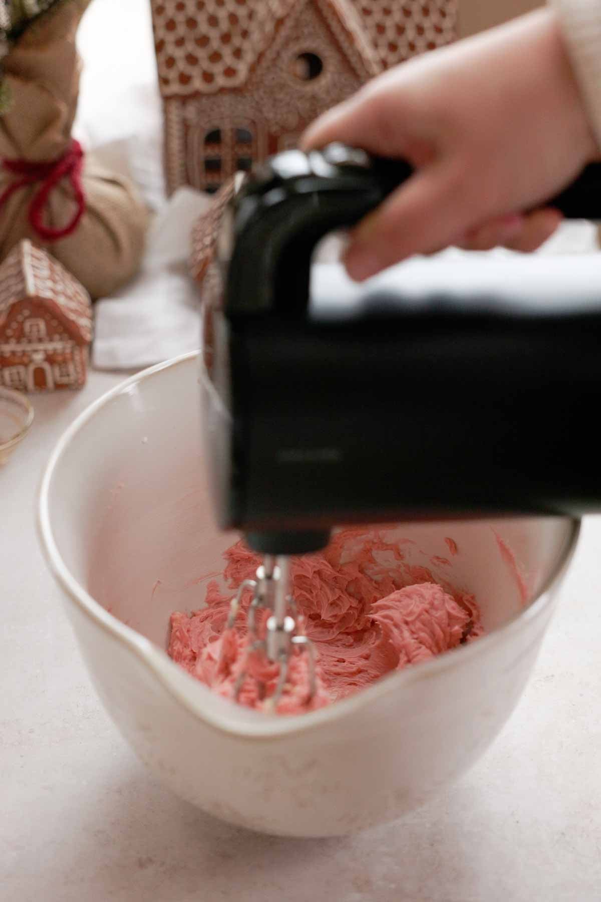 mixing butter and sugar in a large bowl with an electric mixer with pink food coloring