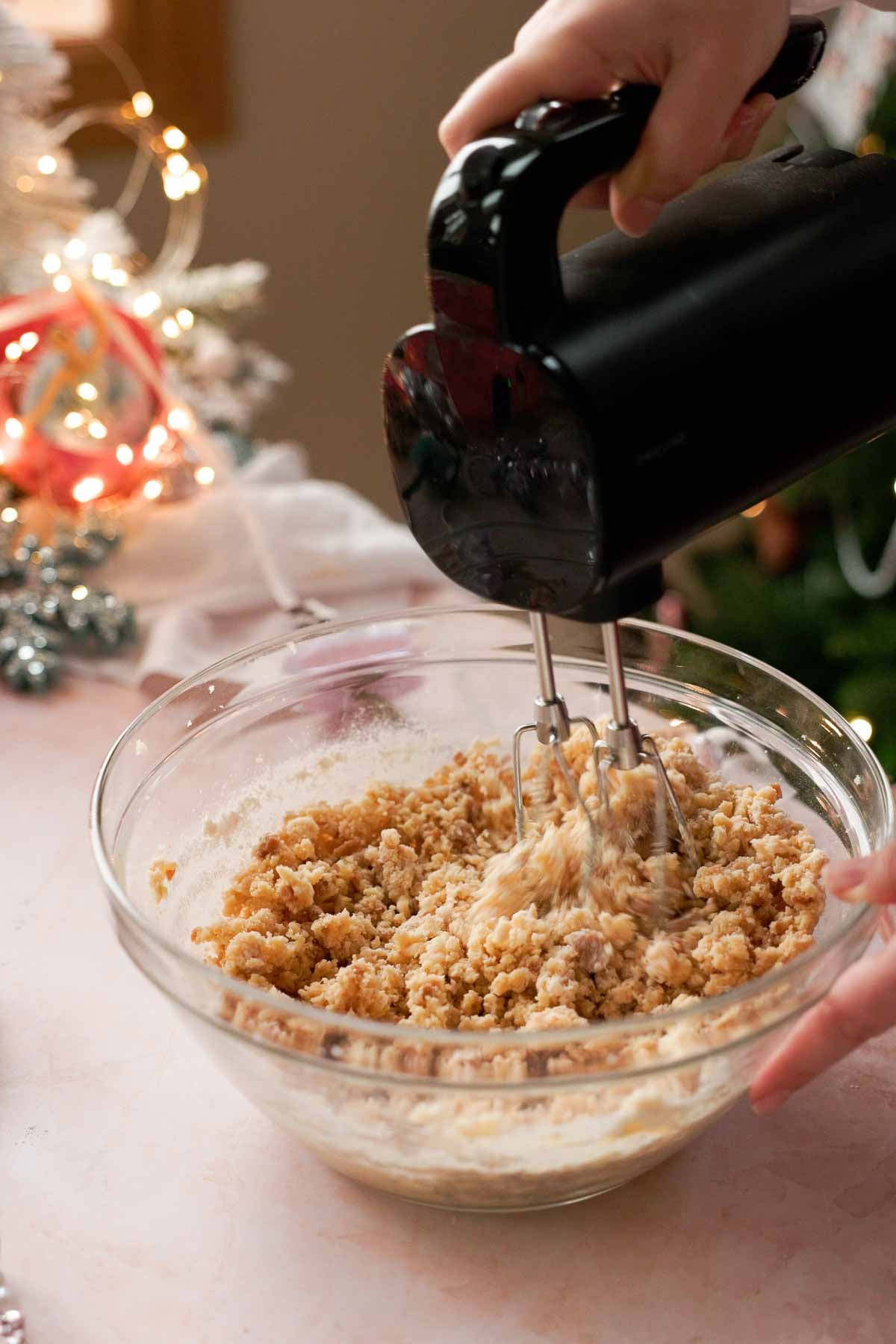 mixing sugar cookie dough with toffee buts in a large glass bowl with an electric mixer