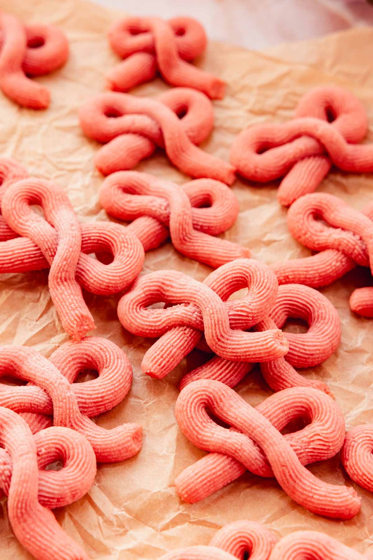 piped butter cookies in the shapes of pink bows on parchment paper