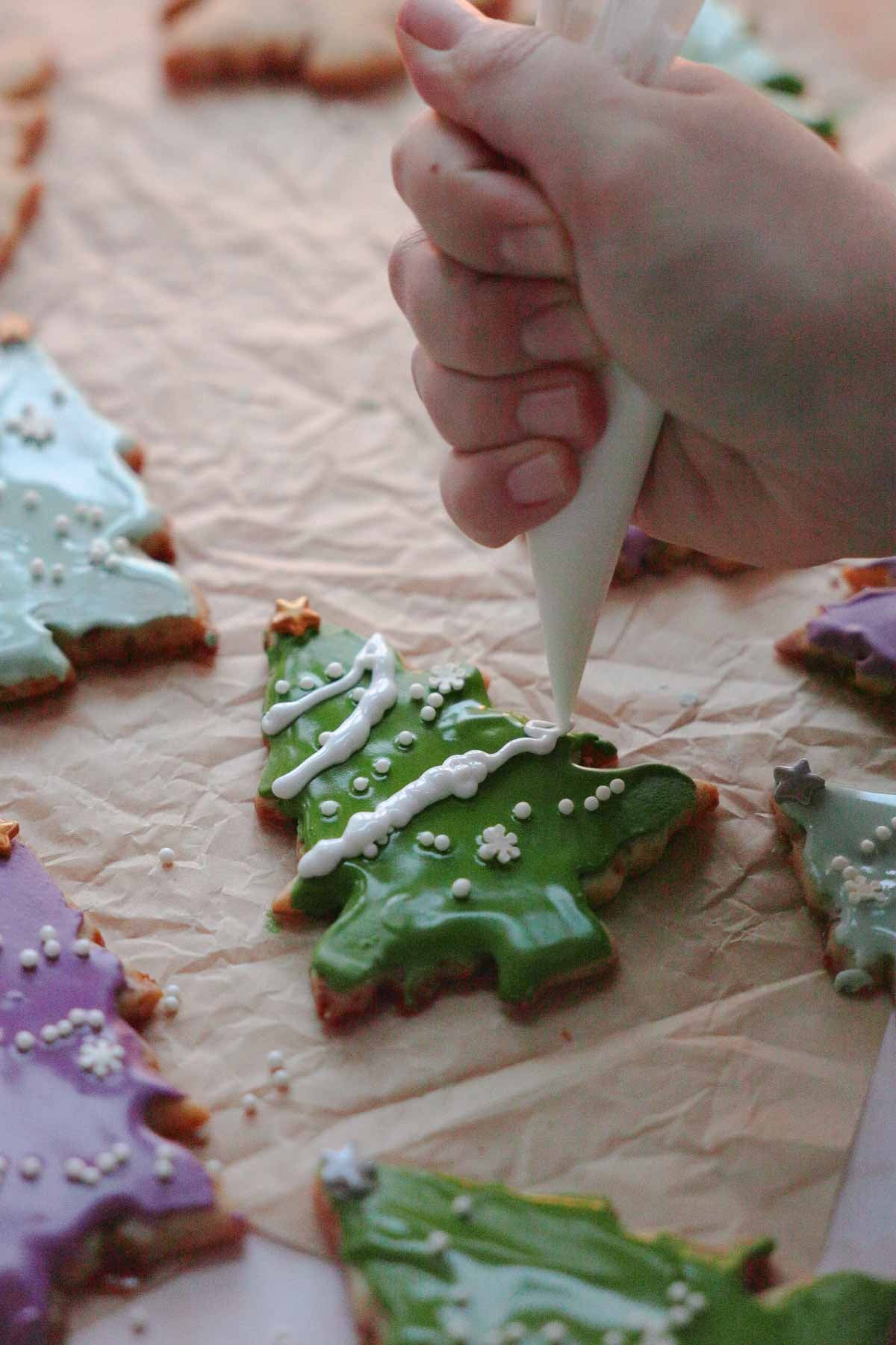 piping snow using white royal icing onto christmas tree sugar cookies