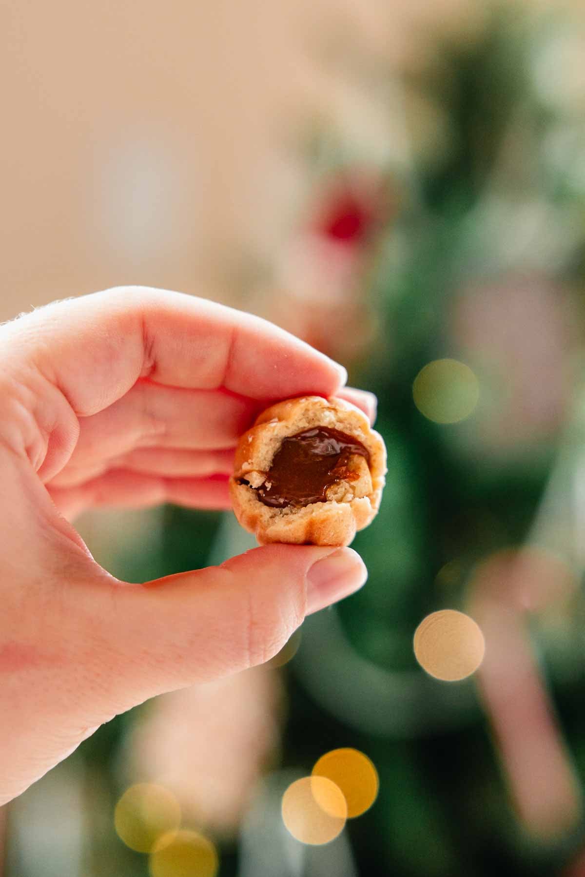 holding up a bitten walnut cookie that is filled with dulce de leche