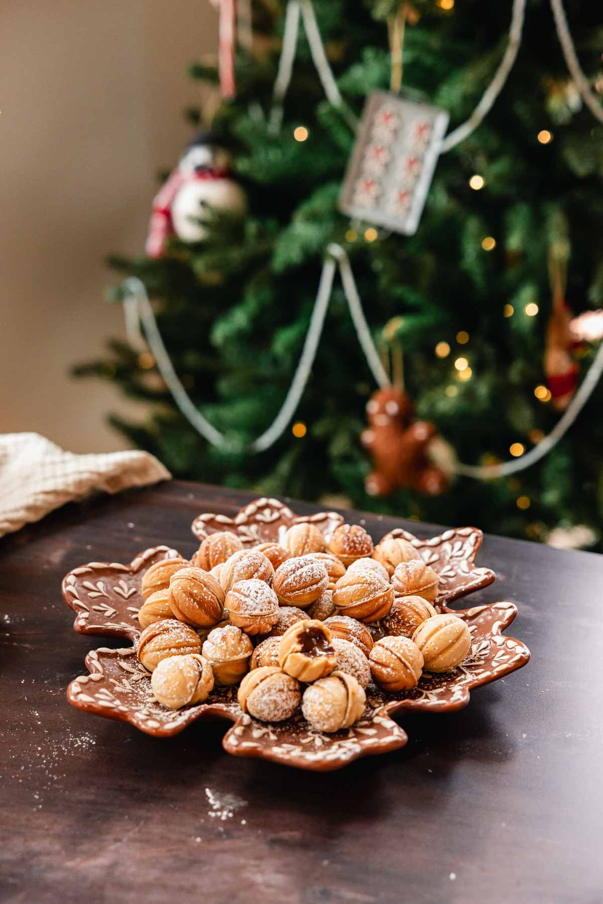 walnut cookies on a plate with Christmas tree in the back