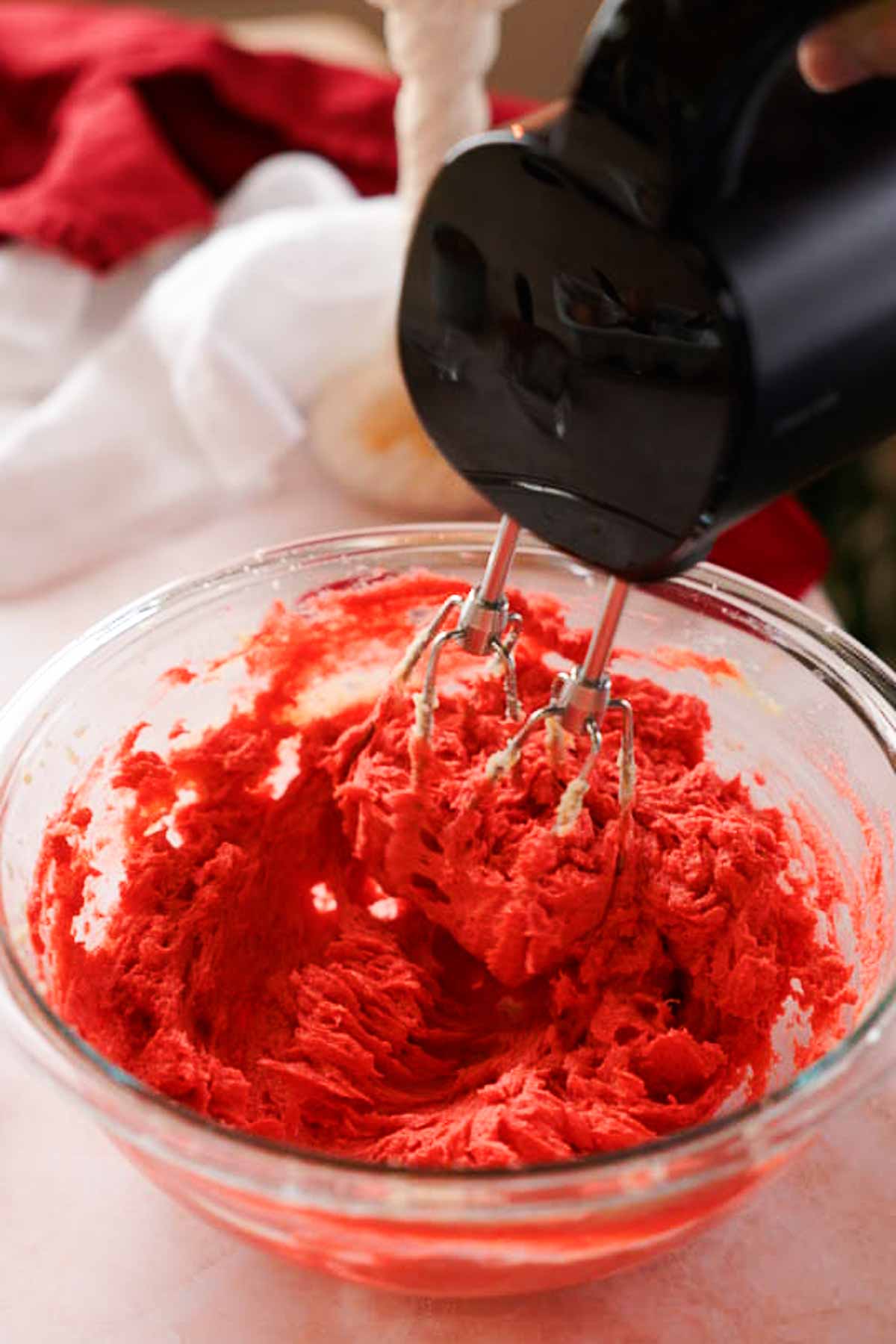 mixing red velvet cookie dough wet ingredients with handheld mixer in glass bowl