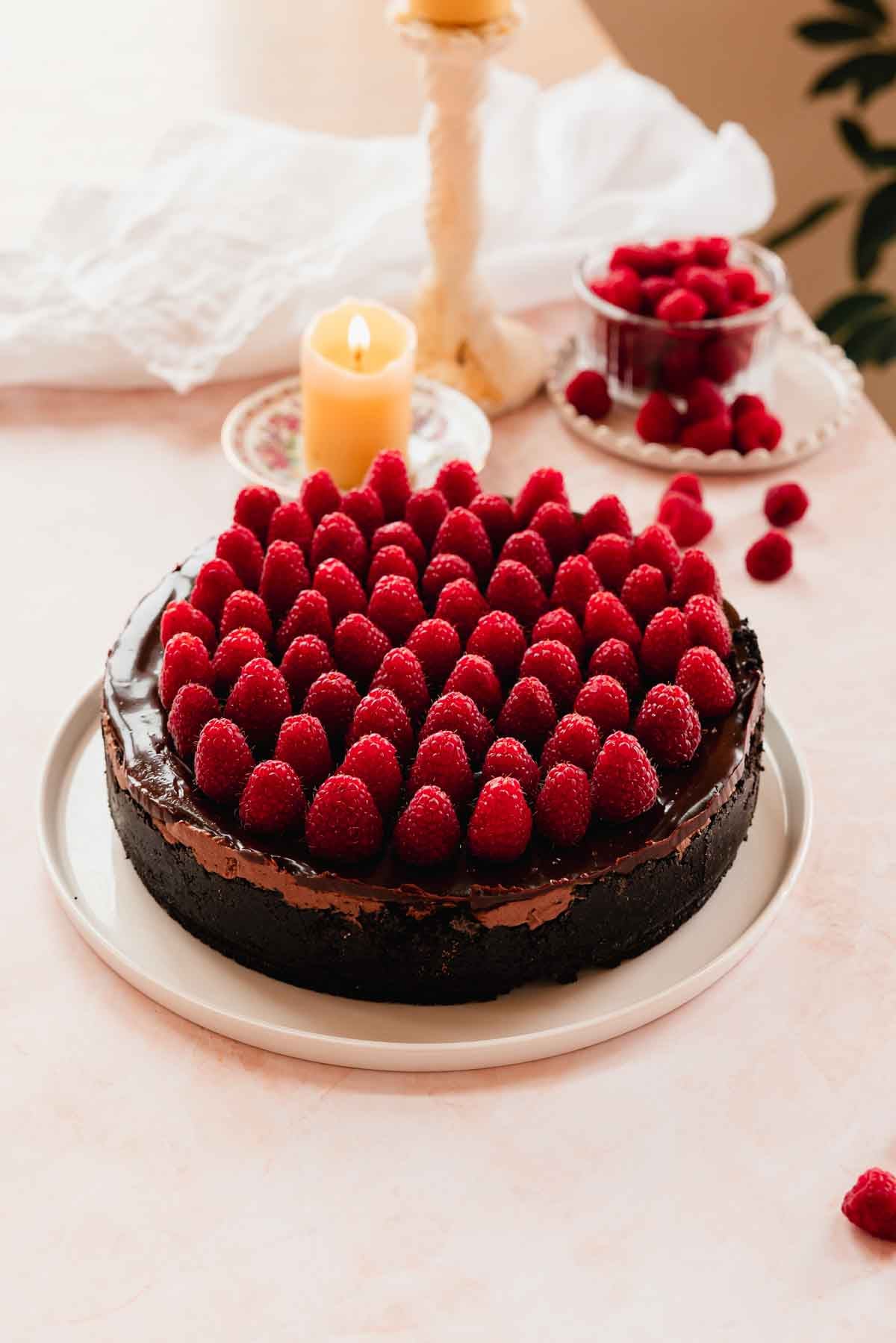chocolate and raspberry cheesecake on a cake plate with spirals of fresh raspberries on top
