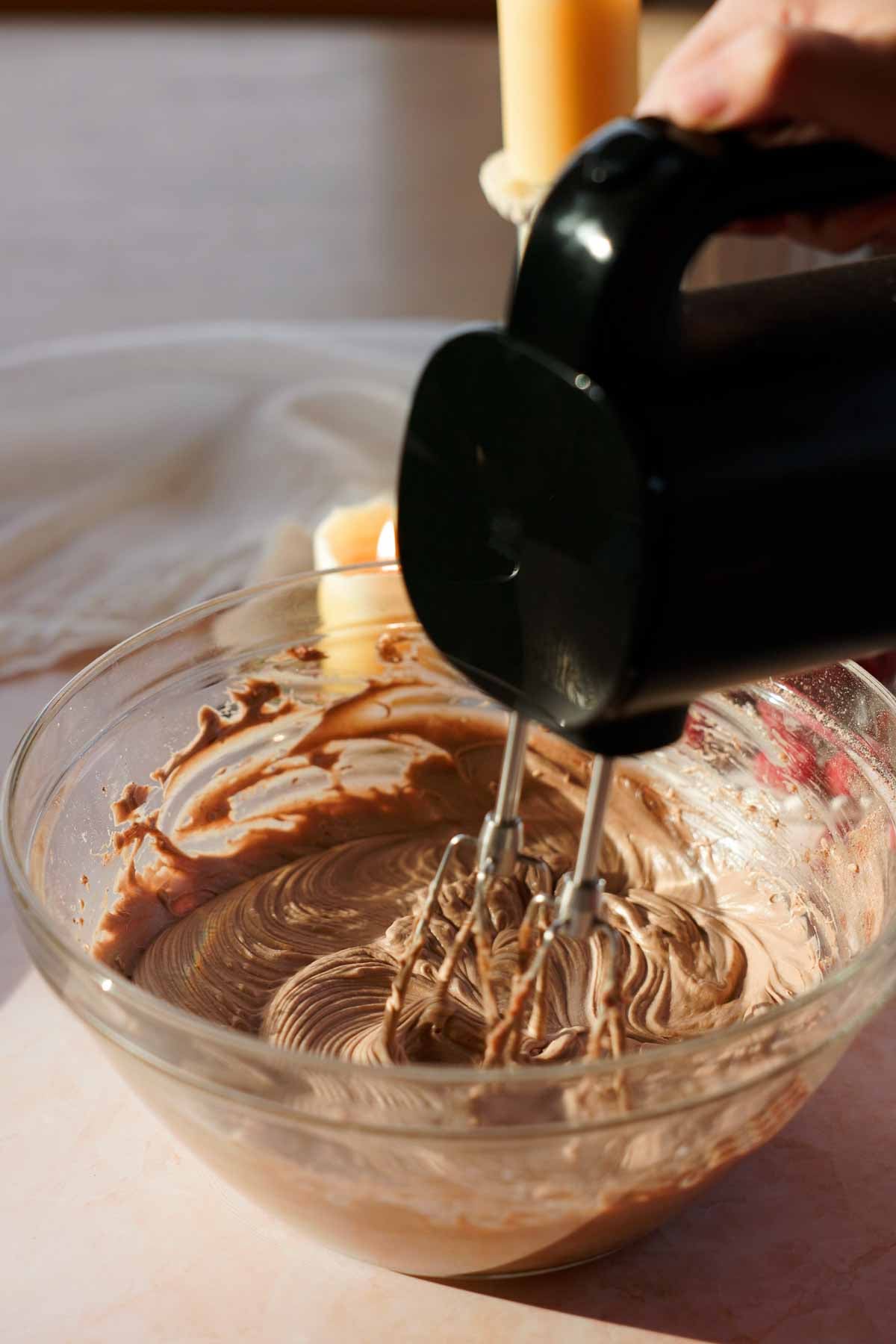 mixing cream cheese with cocoa powder in a glass bowl with electric mixer