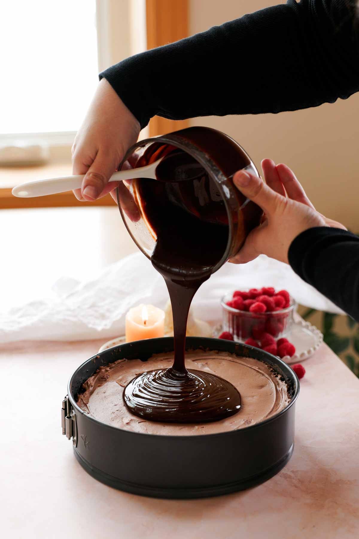 pouring chocolate ganache onto chocolate and raspberry cheesecake