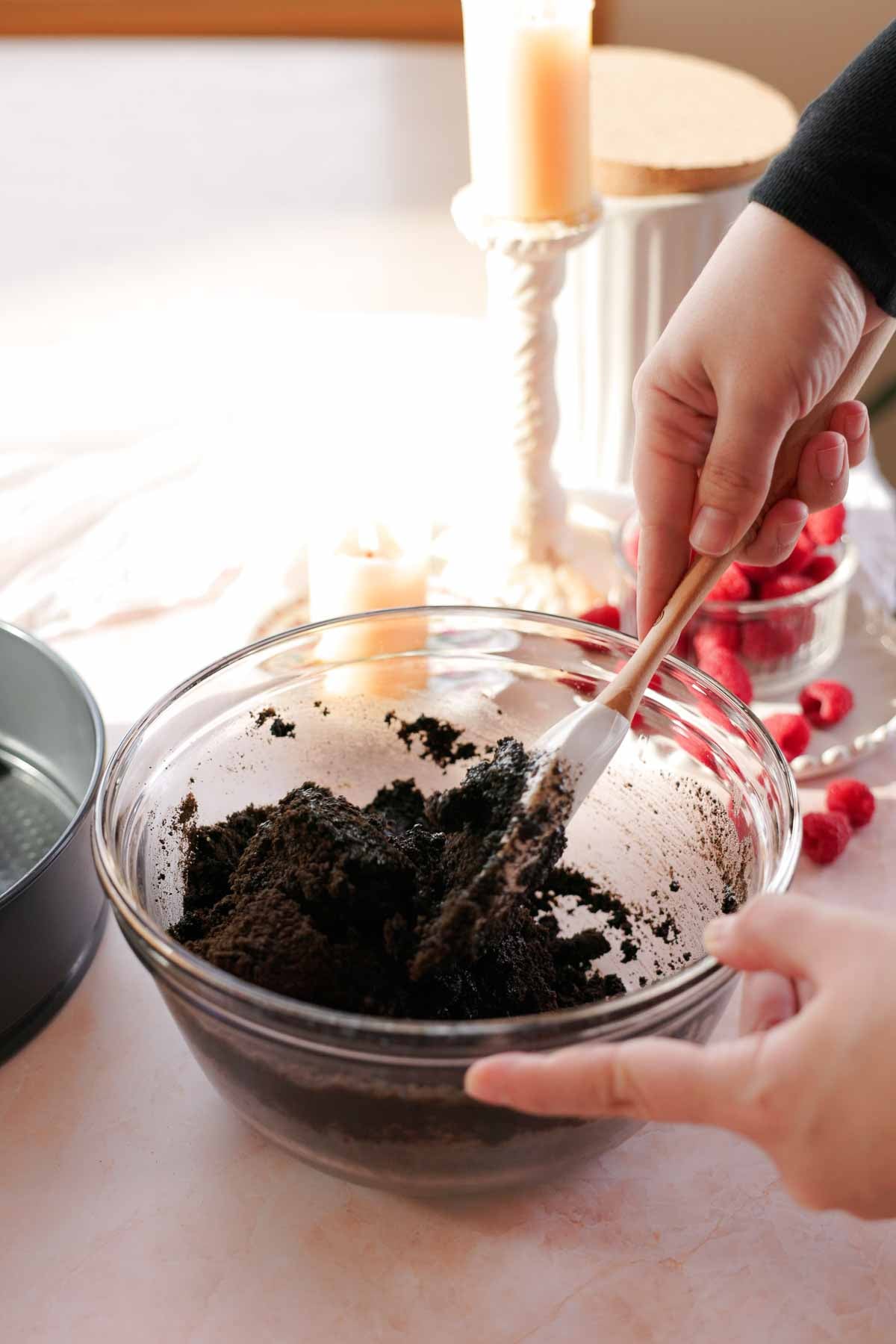 mixing ingredients for chocolate oreo cheesecake crust in a glass bowl with a spatula