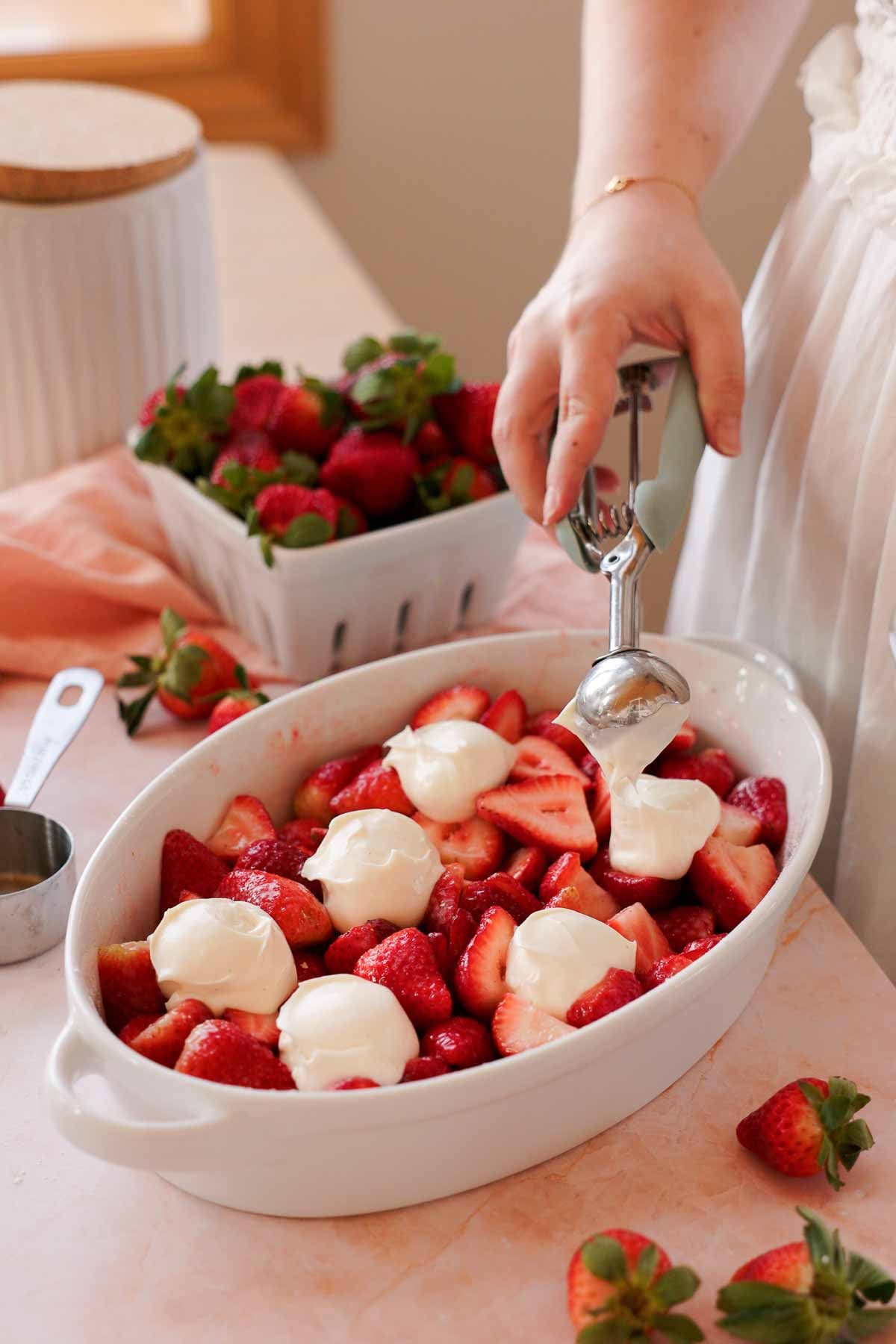 scooping cheesecake filling onto strawberry filling in cobbler pan