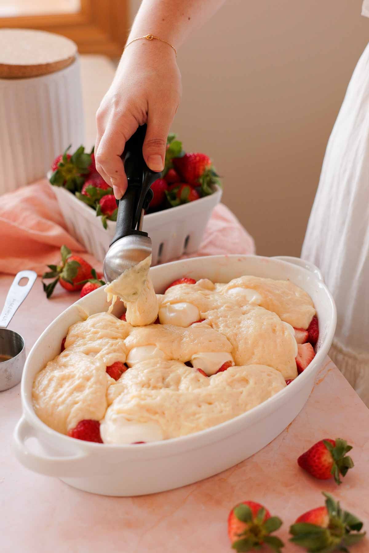 scooping cobbler batter on strawberry cobbler