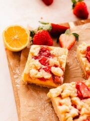 creamy strawberry lemon bars on cutting board with strawberries and lemons