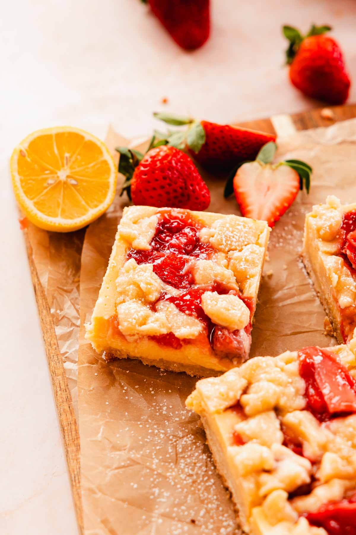 creamy strawberry lemon bars on cutting board with strawberries and lemons