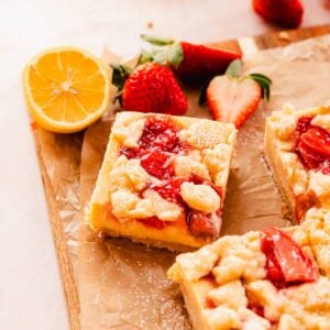 creamy strawberry lemon bars on cutting board with strawberries and lemons