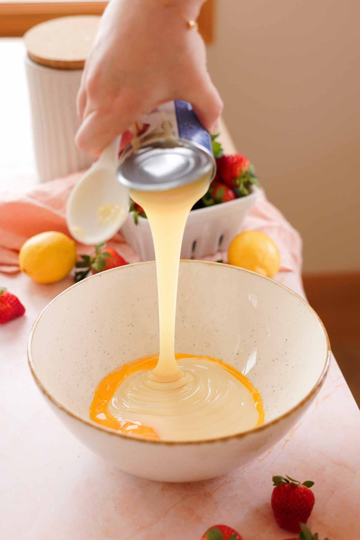 adding sweetened condensed milk into a large bowl with egg yolks