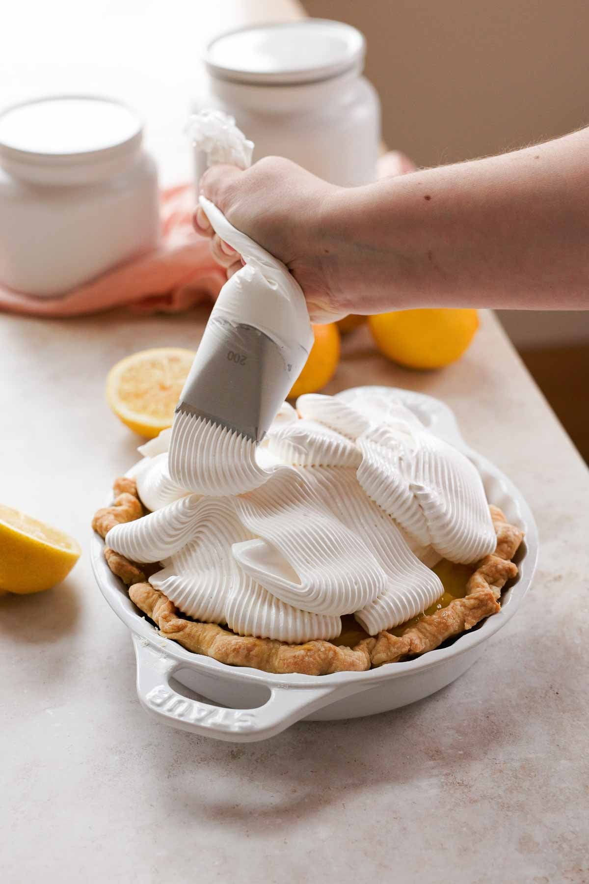 piping meringue with large wide striped piping tip on top of lemon meringue pie