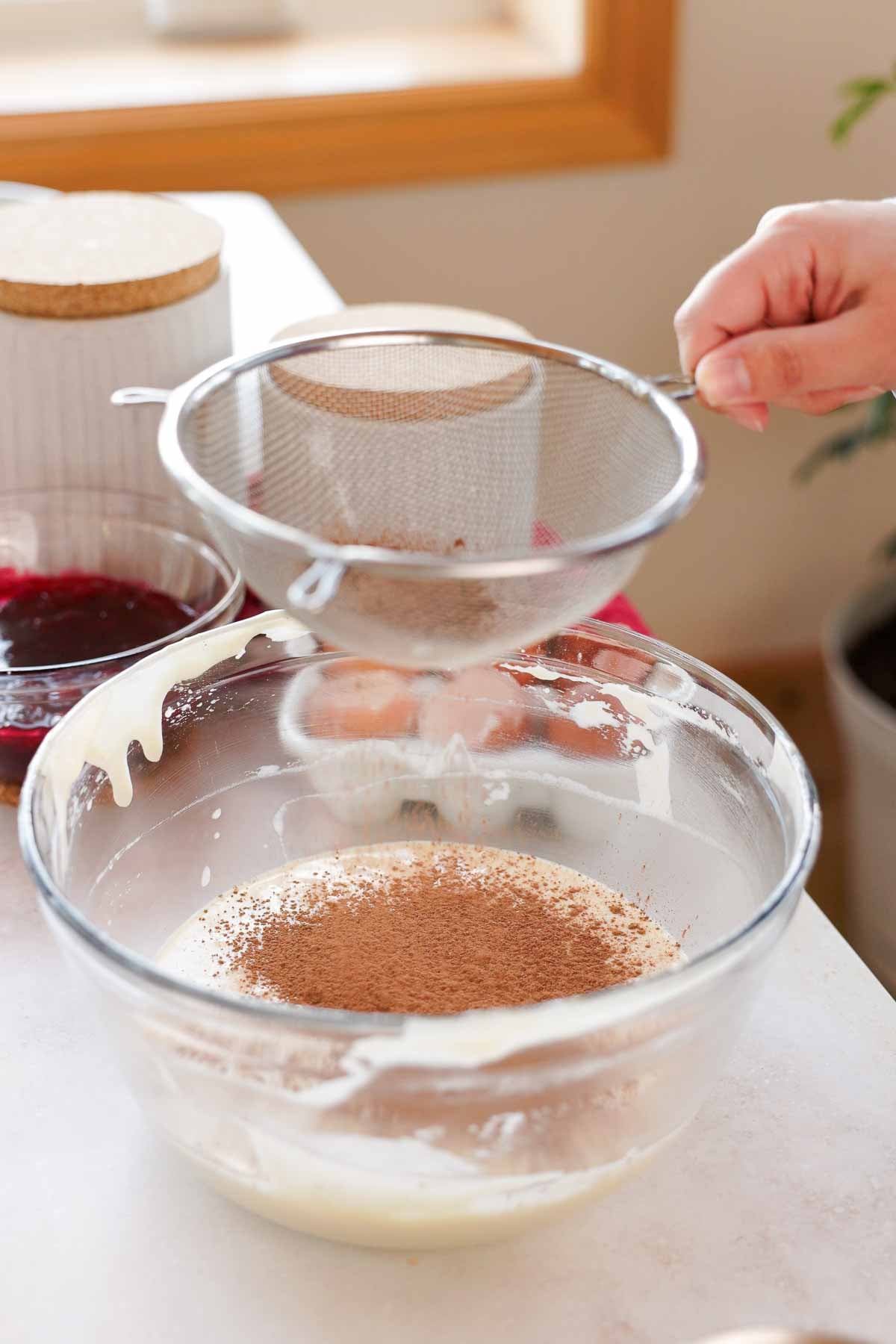 sifting cocoa powder into cake batter in large bowl