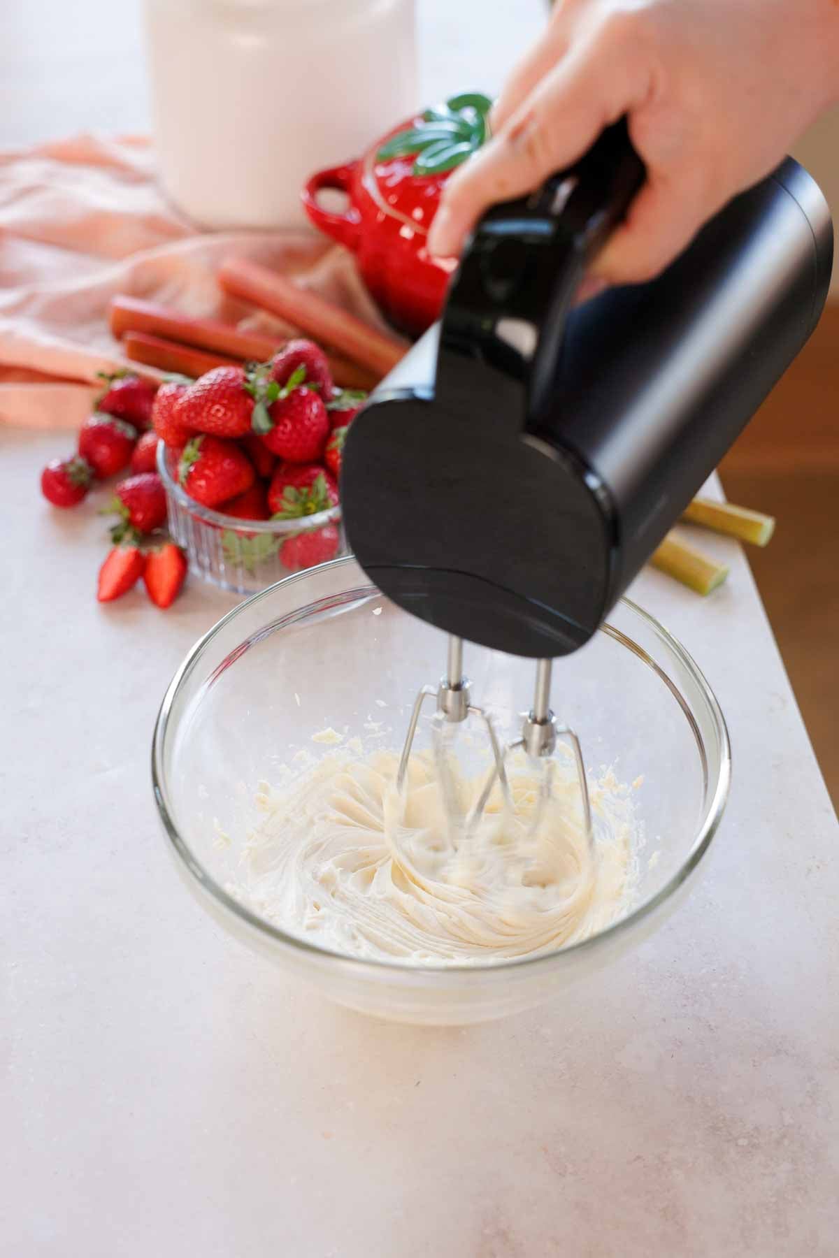 mixing cheesecake filling for cookies with an electric mixer in glass bowl