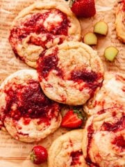 rhubarb cookies on parchment paper with pieces of fresh rhubarb and strawberries