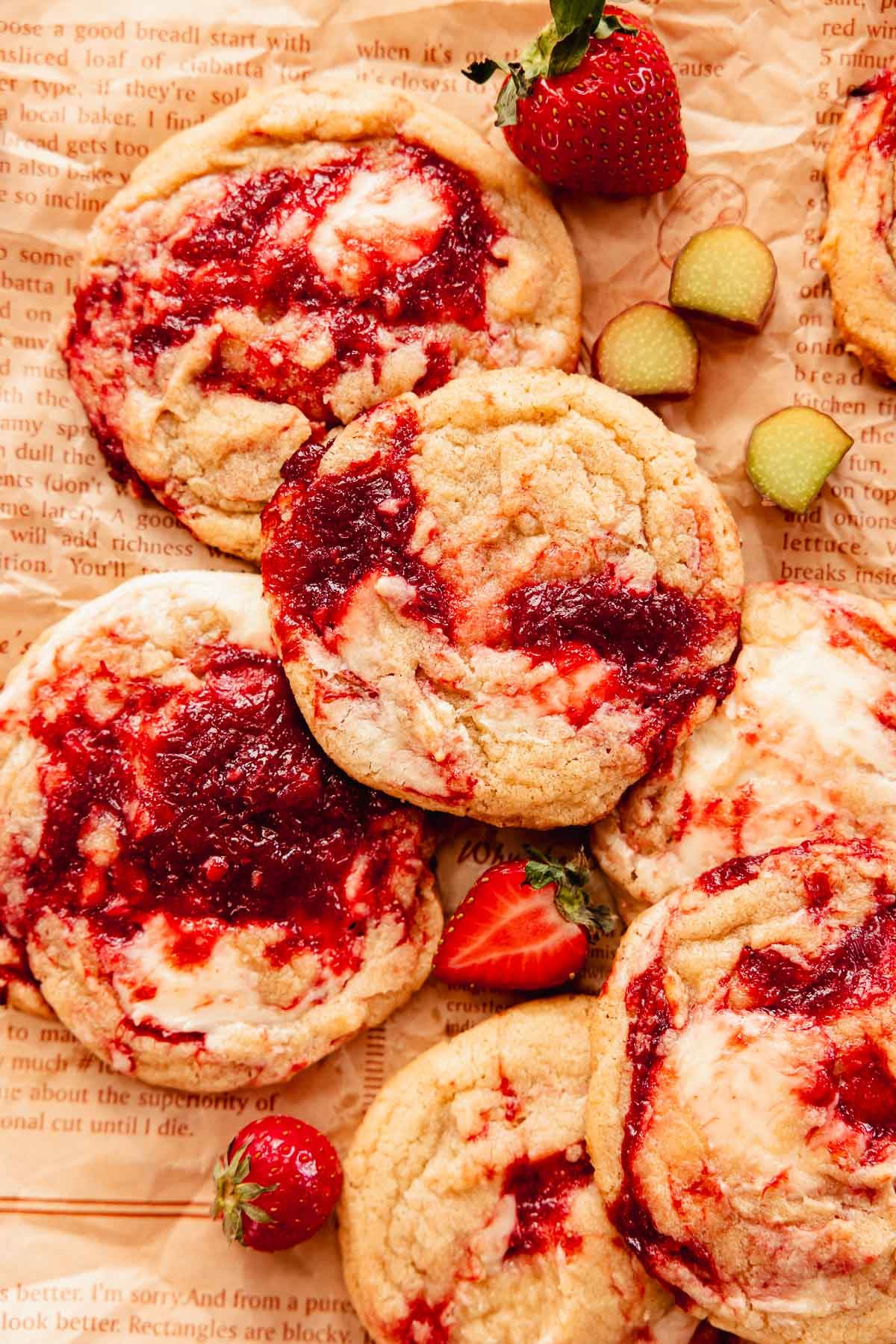 rhubarb cookies on parchment paper with pieces of fresh rhubarb and strawberries