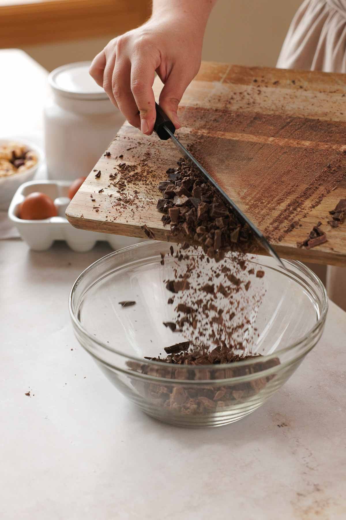 transferring chopped chocolate from a cutting board into a large glass bowl