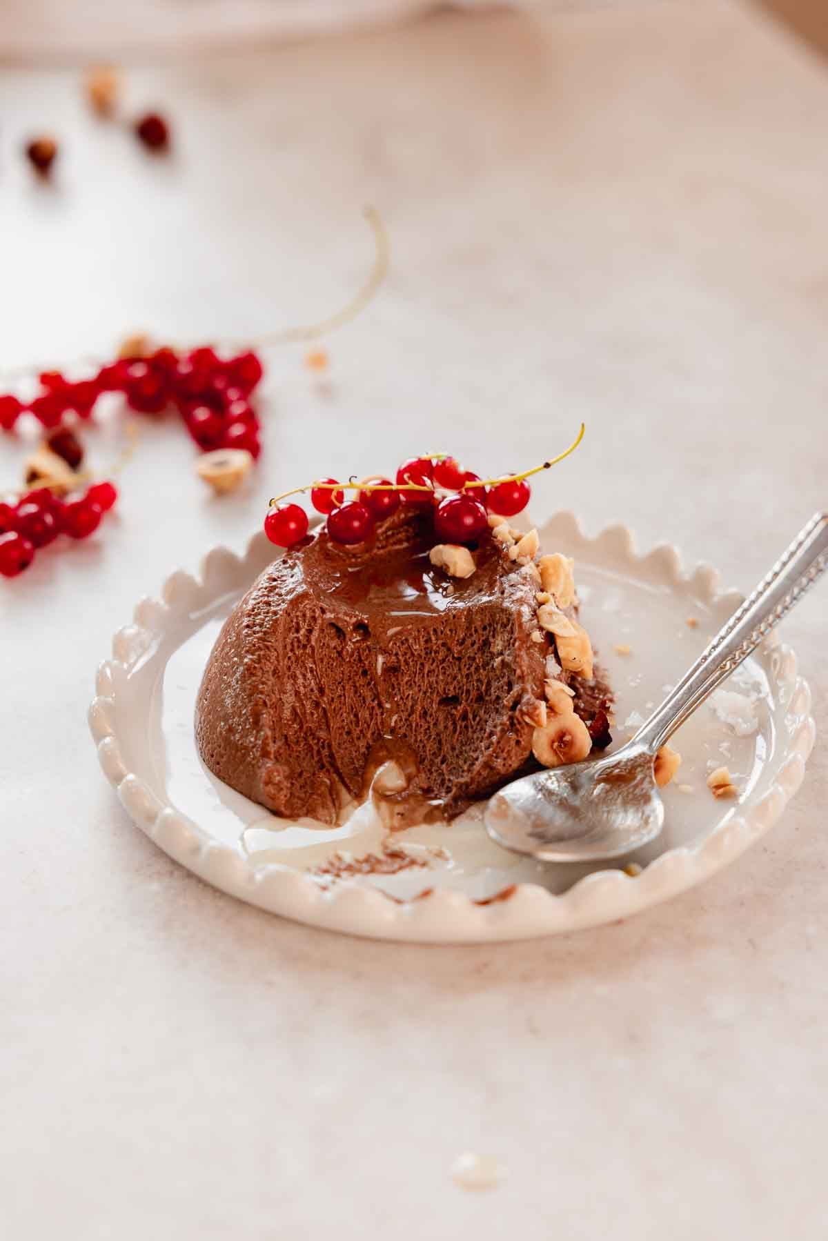 scoop of chocolate hazelnut mousse on plate with red currant and hazelnut pieces
