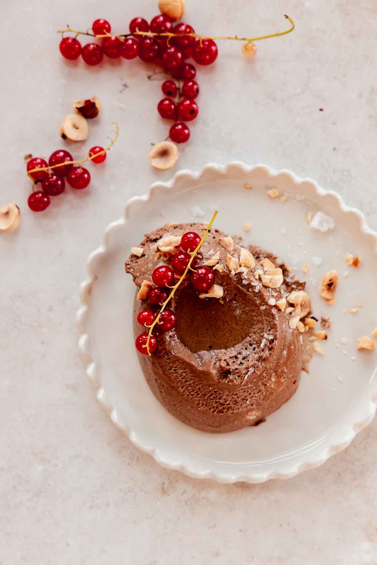 scoop of chocolate hazelnut mousse on a plate with chopped hazelnuts, red currant berries, and oil