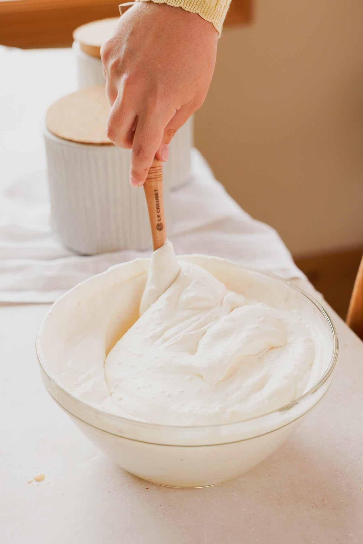folding toasted coconut no churn ice cream with a spatula in a large glass bowl.