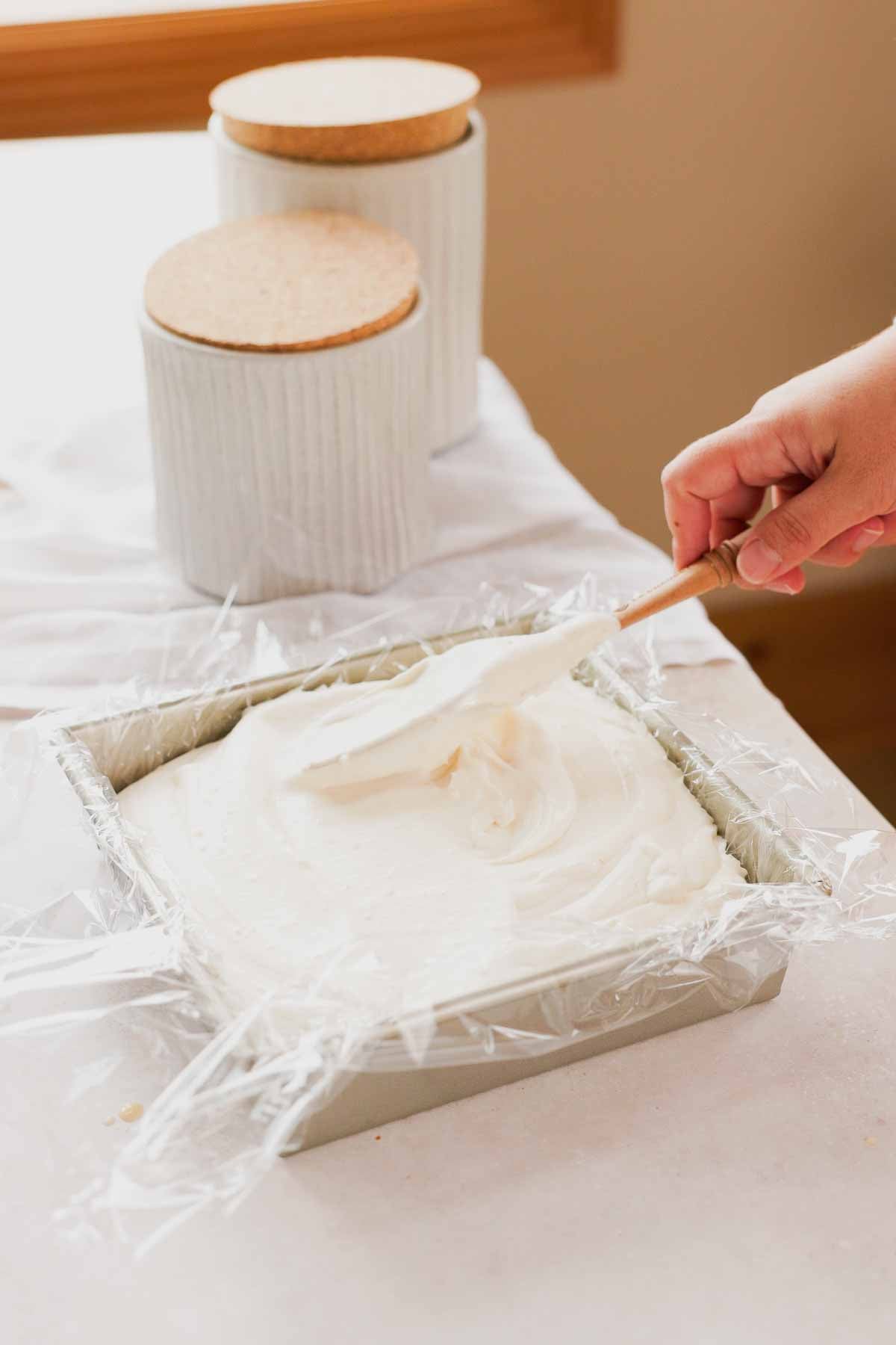 transferring toasted coconut no churn ice cream into plastic wrap lined square baking pan
