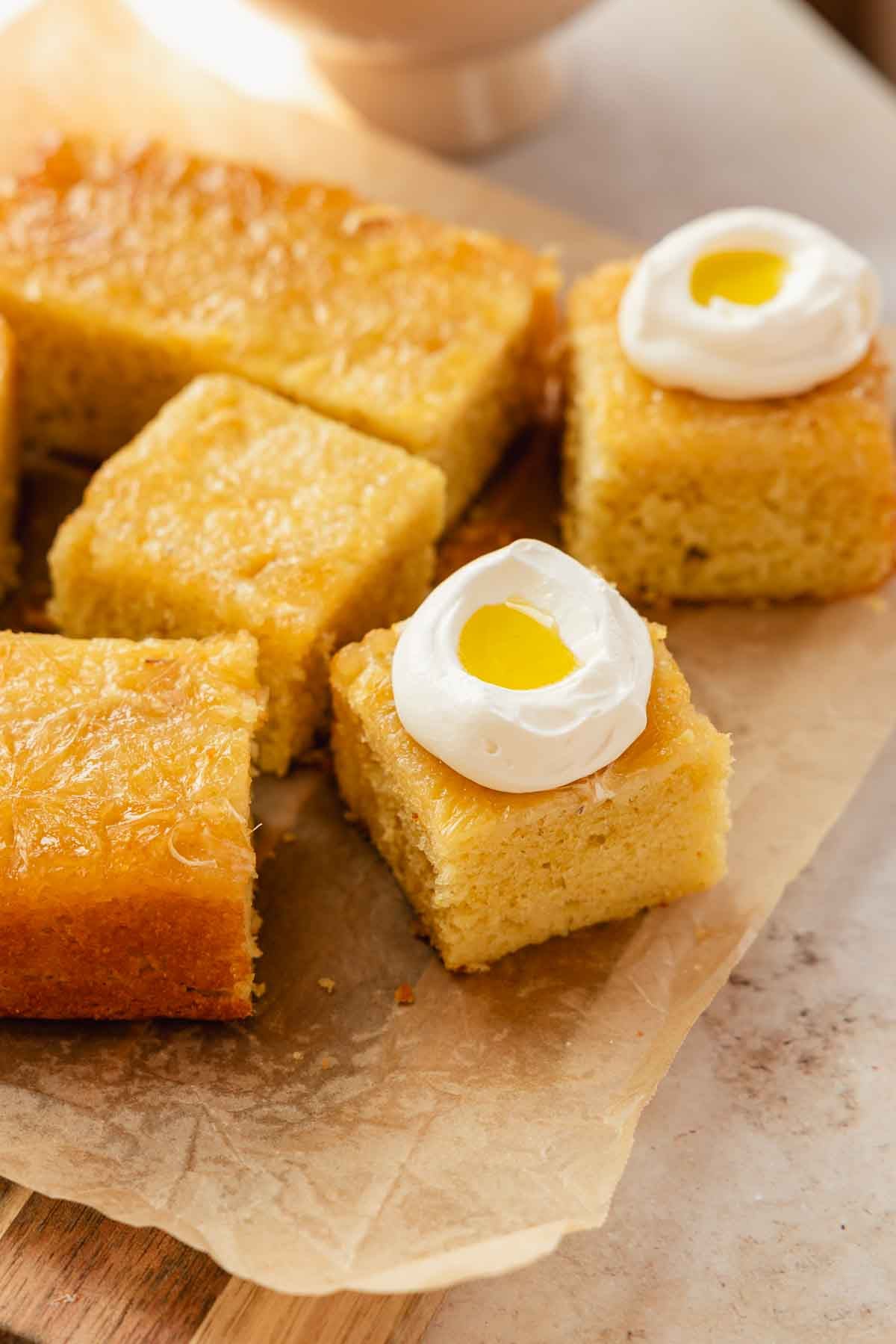slices of upside down lemon olive oil cake on a piece of parchment paper with dollops of whipped cream and olive oil